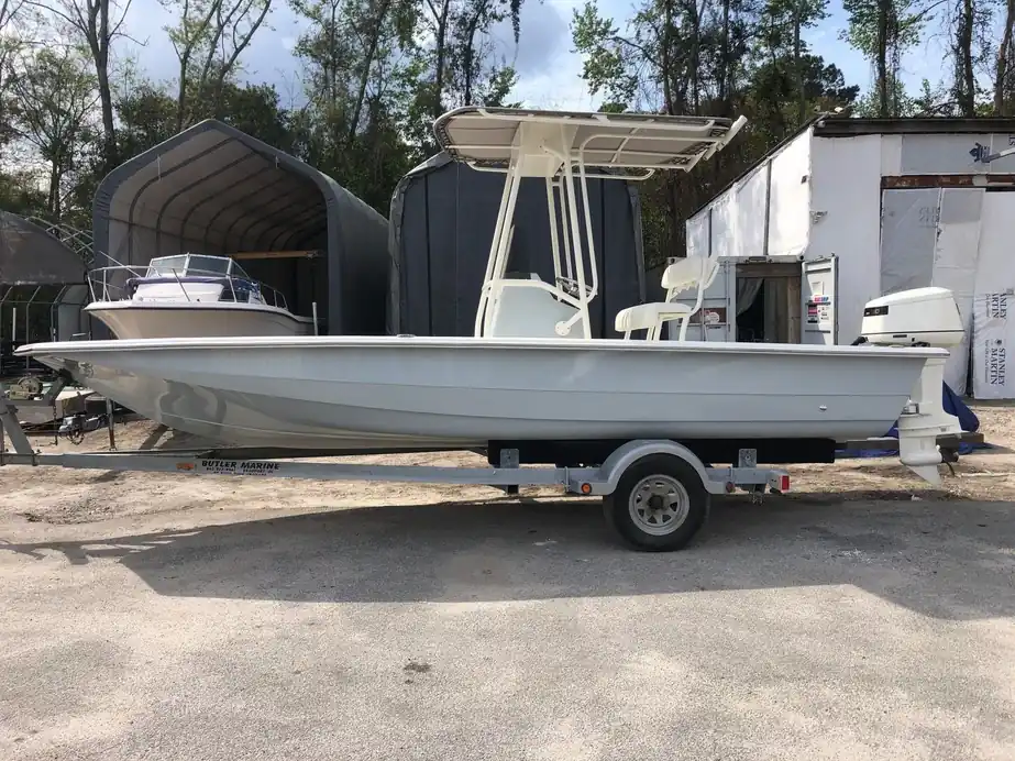 White bay boat with a T-top on a single-axle trailer with shed bays behind