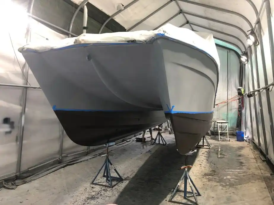 Catamaran hulls on stands in the tent, the boot line taped over fresh bottom paint