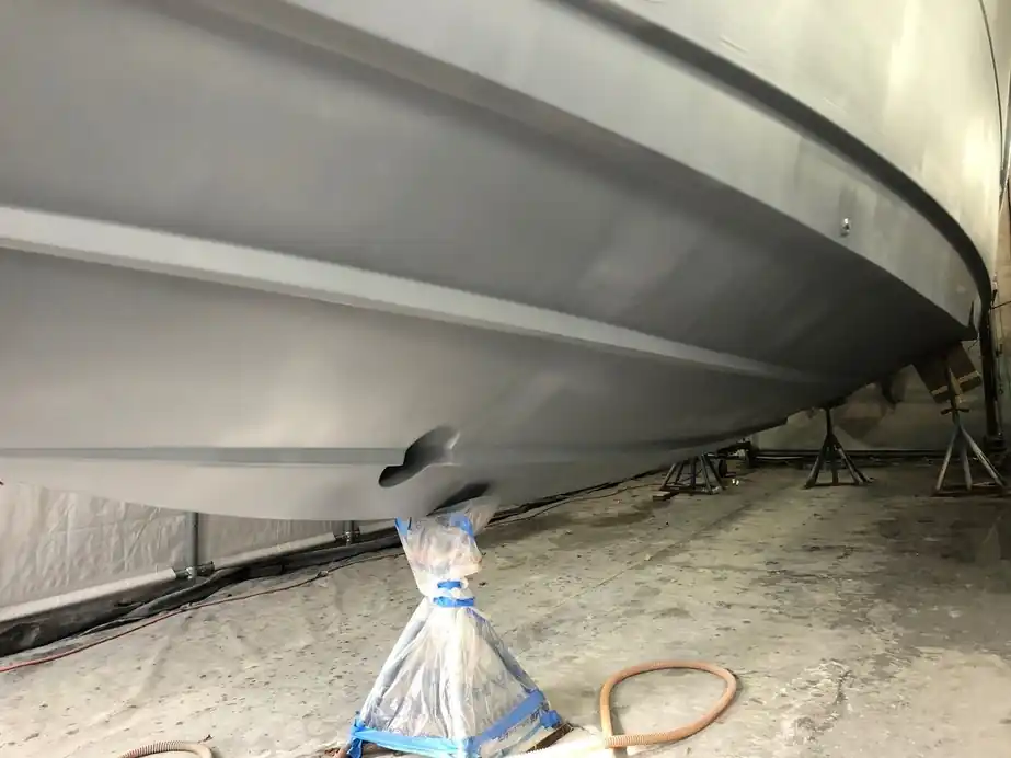 A primed grey hull bottom on stands inside the paint tent, the outdrive bagged