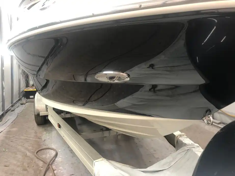 A navy-painted hull in the paint bay, the shop lights reflected in the gloss