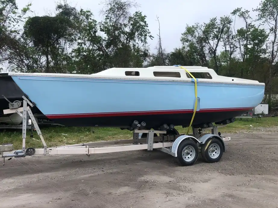 A pale-blue sailboat hull on a trailer with a new red boot stripe above dark bottom paint