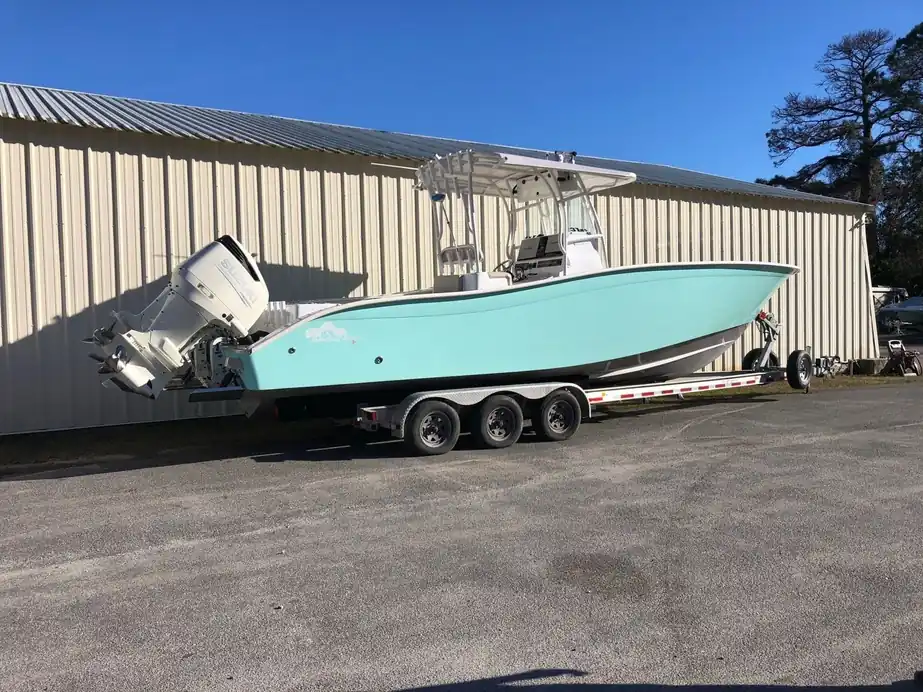 A seafoam-green center console on a triple-axle trailer in front of the shop building