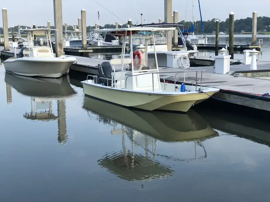 Cream center console and skiff tied at the dock with flat water reflections